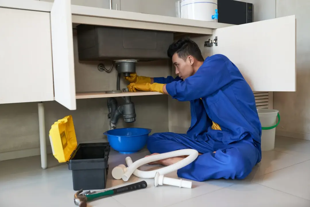 Plumber clearing a blocked waste trap under a kitchen sink