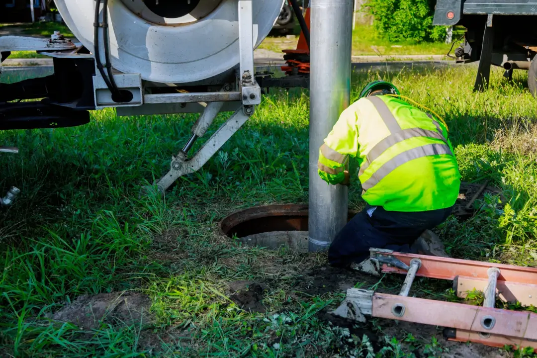 Engineer lowering a high-pressure drain jetting hose into a manhole