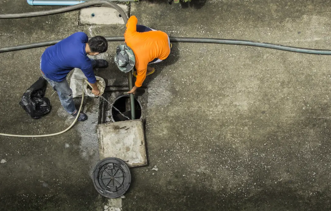 Two drainage engineers clearing a blocked drain chamber with a jetting hose