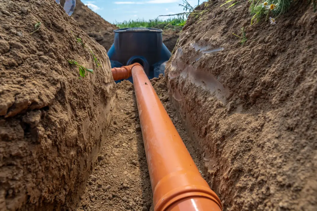 New orange drain pipe laid in an excavated trench